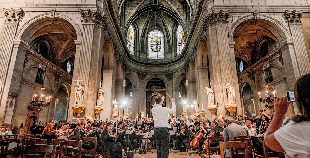 Orchestra performing in St Sulpice Church, Paris, with conductor leading musicians.