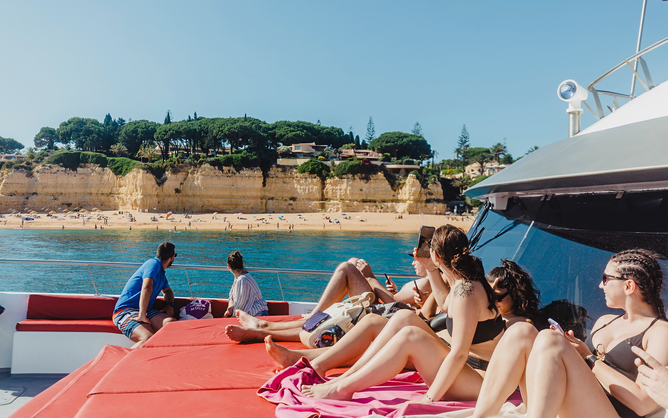 Tourists relaxing on a boat near the sandy beach and cliffs of Benagil Caves, Algarve, Portugal.