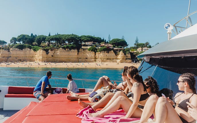 Tourists relaxing on a boat near the sandy beach and cliffs of Benagil Caves, Algarve, Portugal.