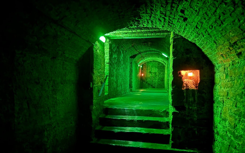 Dimly lit stone corridor in Edinburgh Vaults with green lighting.