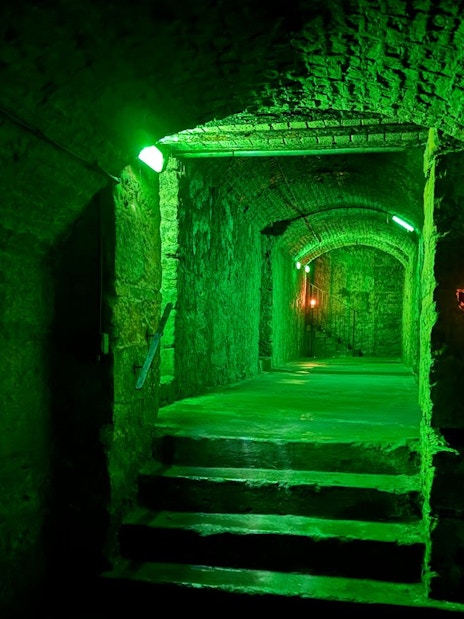 Dimly lit stone corridor in Edinburgh Vaults with green lighting.