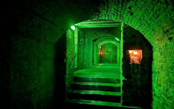 Dimly lit stone corridor in Edinburgh Vaults with green lighting.