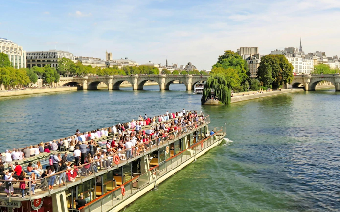 Seine River cruise boat with tourists near Paris bridges and cityscape.