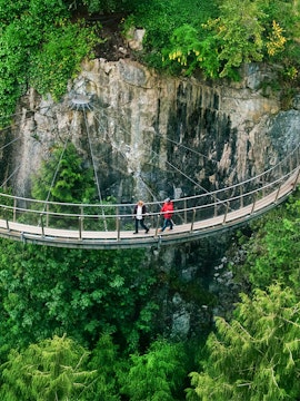 Visitors walking on Capilano Suspension Bridge, North Vancouver, surrounded by lush greenery.