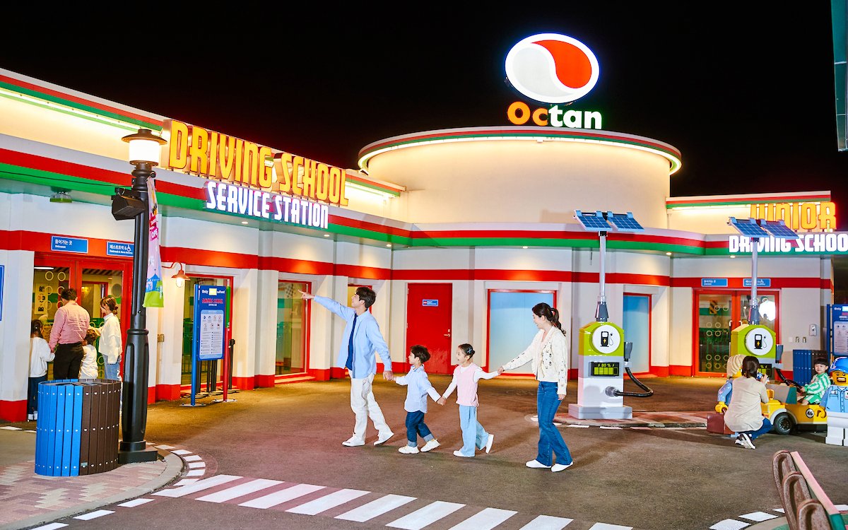 Family at Legoland driving school attraction with children learning to drive toy cars.