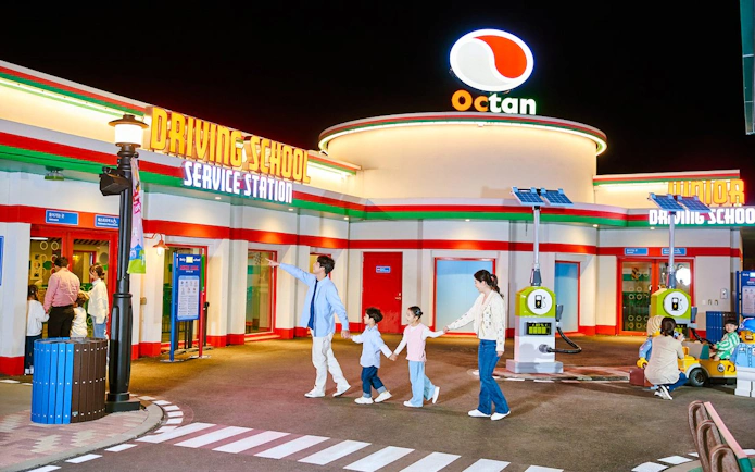 Family at Legoland driving school attraction with children learning to drive toy cars.