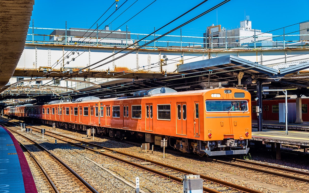 Orange local train at an Osaka station platform under clear blue sky.
