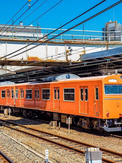 Orange local train at an Osaka station platform under clear blue sky.