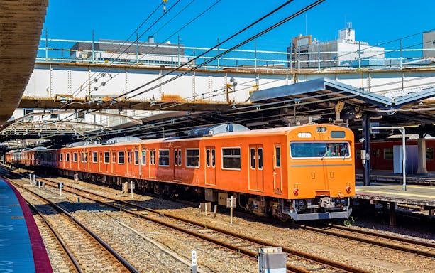 Orange local train at an Osaka station platform under clear blue sky.