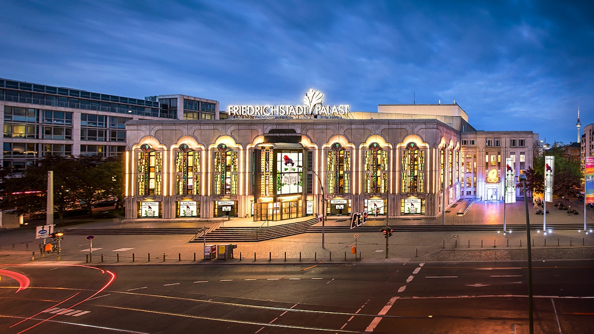 Beleuchtete Außenansicht des Friedrichstadt-Palasts in Berlin bei Abenddämmerung.