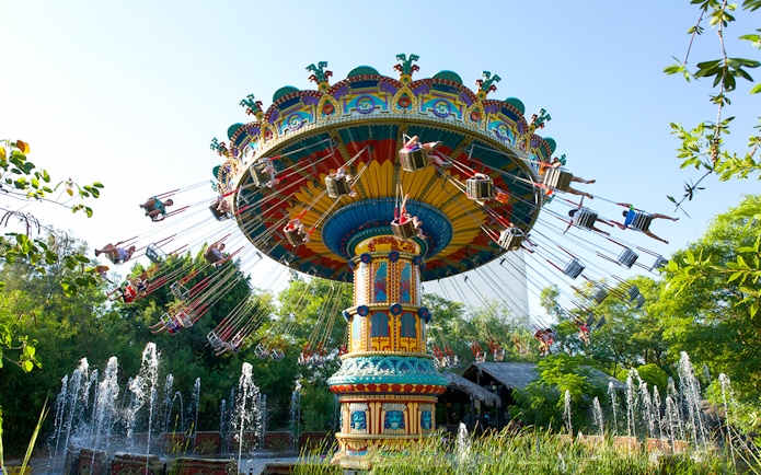 Swing ride at Isla Magica's The Flight of the Falcon, surrounded by trees and fountains.