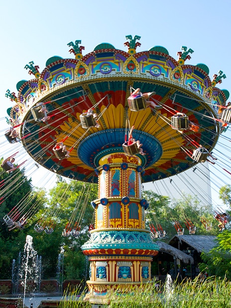Swing ride at Isla Magica's The Flight of the Falcon, surrounded by trees and fountains.
