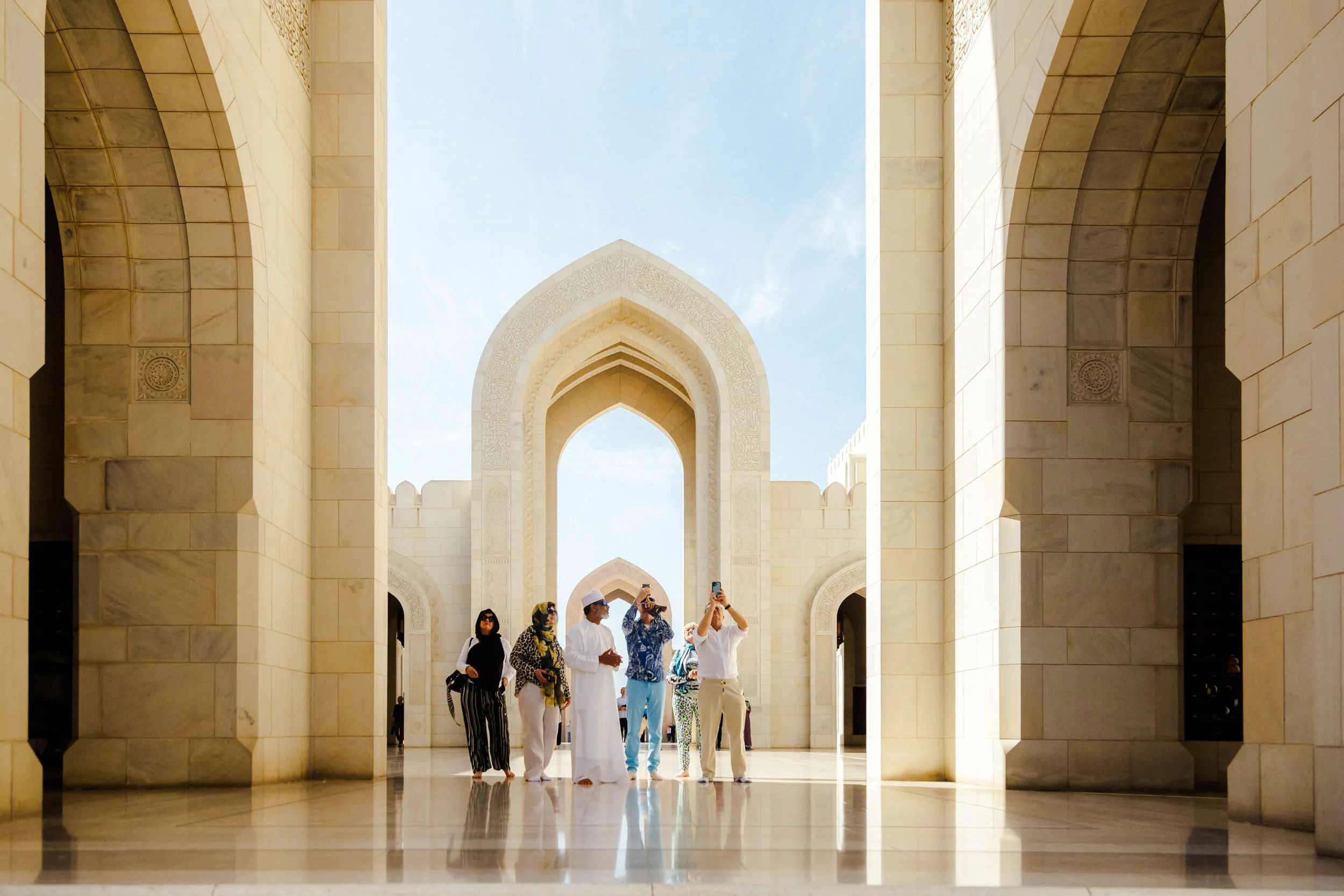 Visitors exploring the architecture of Sultan Qaboos Grand Mosque in Muscat.