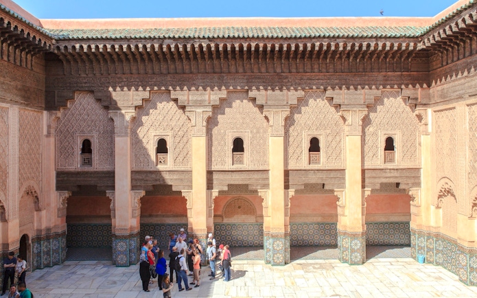 Courtyard of Ben Youssef Madrasa in Marrakech with intricate carvings and tourists exploring.