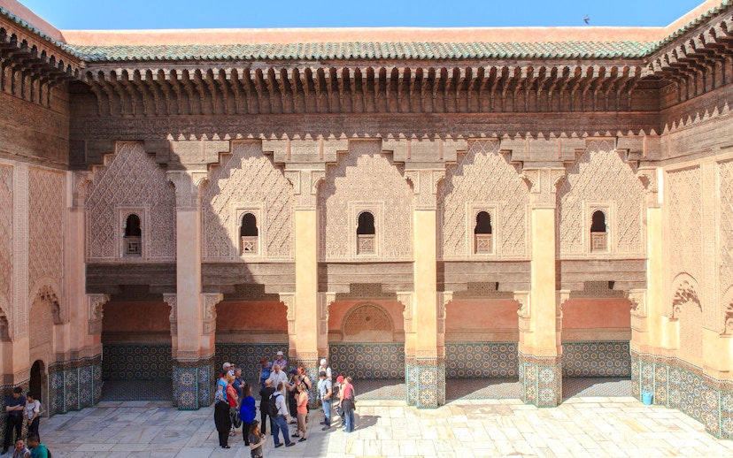 Courtyard of Ben Youssef Madrasa in Marrakech with intricate carvings and tourists exploring.