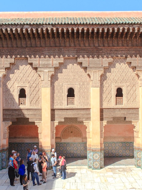 Courtyard of Ben Youssef Madrasa in Marrakech with intricate carvings and tourists exploring.