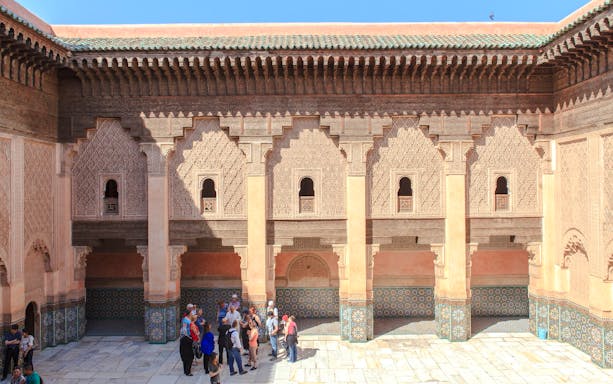 Courtyard of Ben Youssef Madrasa in Marrakech with intricate carvings and tourists exploring.