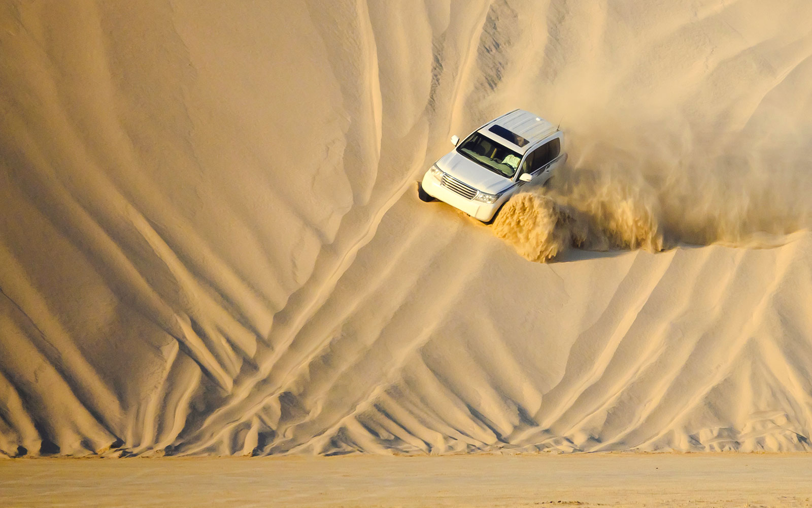 SUV descending sand dune during dune bashing in Doha.