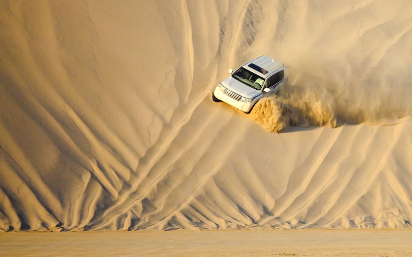 SUV descending sand dune during dune bashing in Doha.