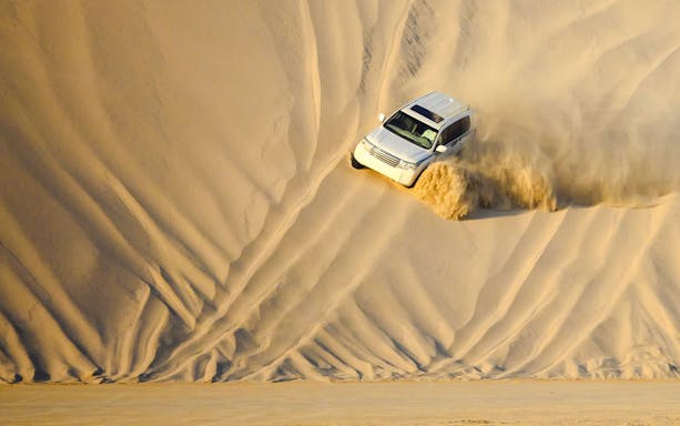 SUV descending sand dune during dune bashing in Doha.