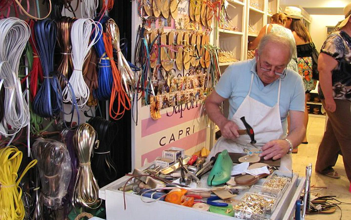 Craftsman creating custom sandals in a Capri, Italy shop with tools and materials.