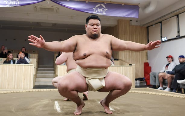 Sumo wrestler crouches in preparation for a match in a Tokyo arena.