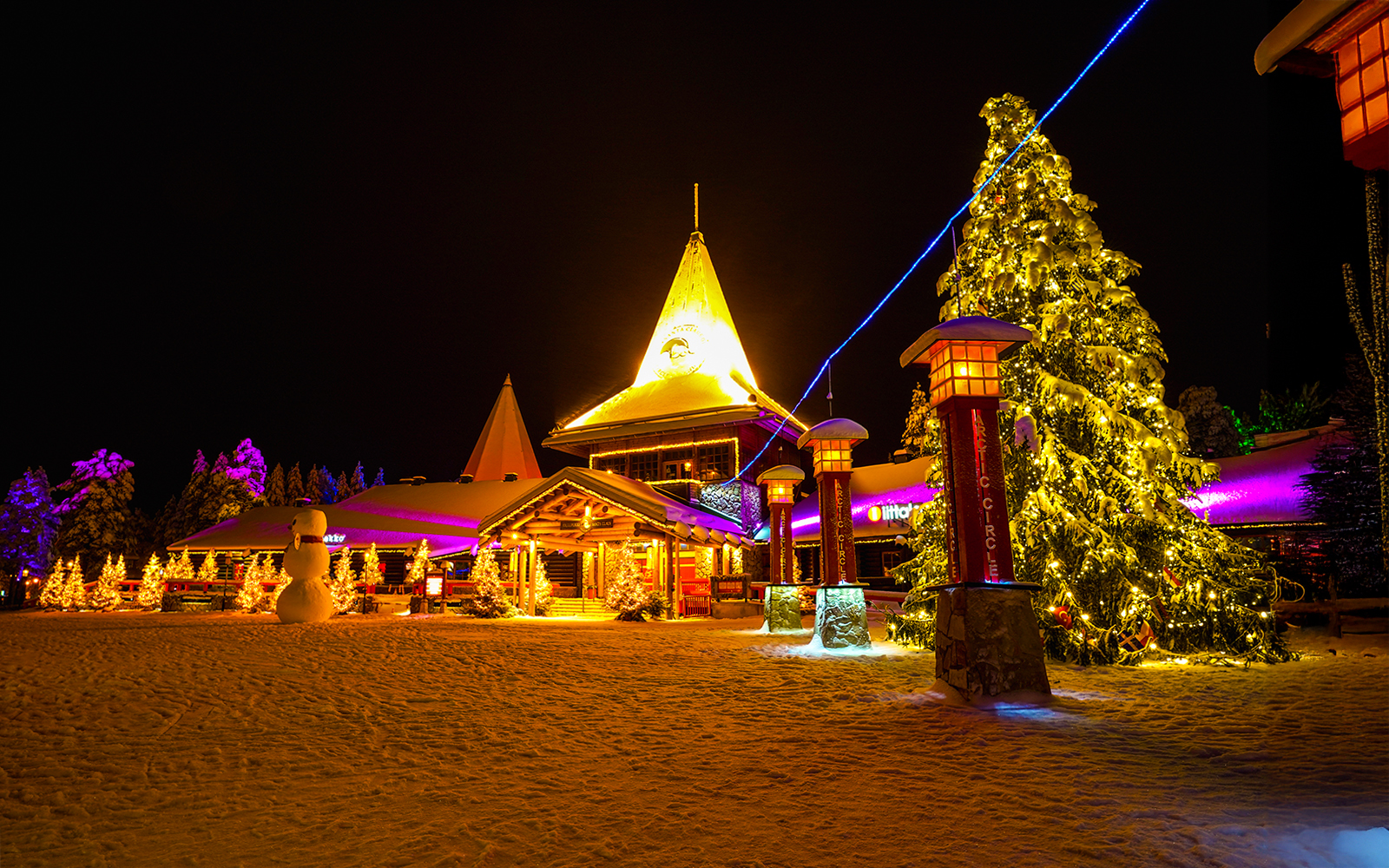 Santa Claus Village in Rovaniemi illuminated at night with snow-covered trees and festive lights.