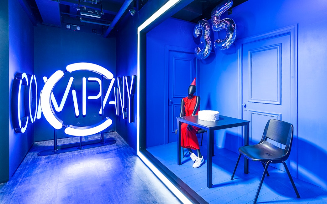 Neon "Company" sign and mannequin in red dress with cake at Museum of Broadway exhibit.