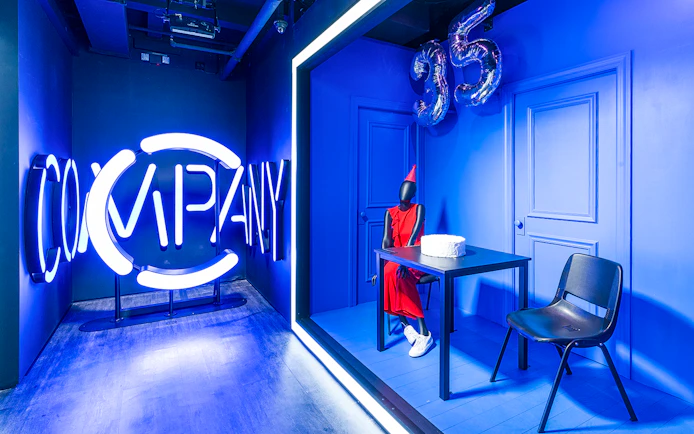 Neon "Company" sign and mannequin in red dress with cake at Museum of Broadway exhibit.