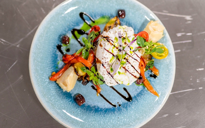 Burrata with roasted vegetables and balsamic glaze on a blue plate, served on THEO Boat Brunch cruise in Paris.