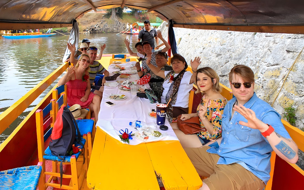 Guests waving on a Trajinera party boat in Xochimilco, Mexico.