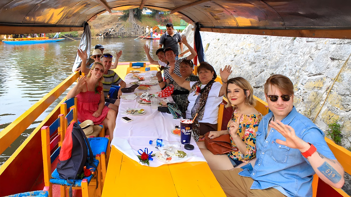 Guests on Trajinera party boat in Xochimilco, Mexico, enjoying vibrant canal tour.