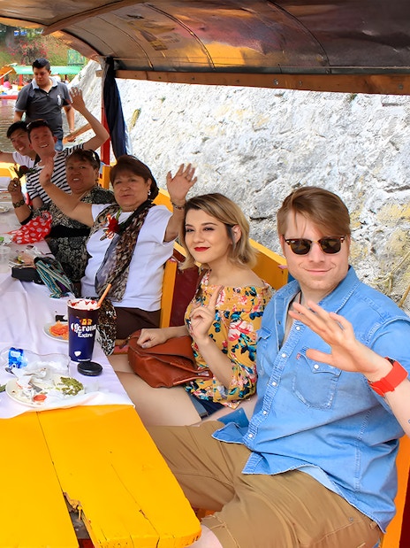 Guests waving on a Trajinera party boat in Xochimilco, Mexico.