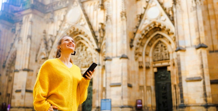 Visitor using audio guide at Prague Castle entrance.