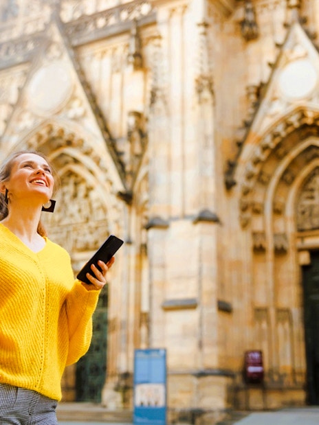 Visitor using audio guide at Prague Castle entrance.