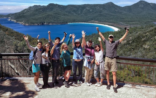 Tour group celebrating at Wineglass Bay lookout with ocean and mountains in background.