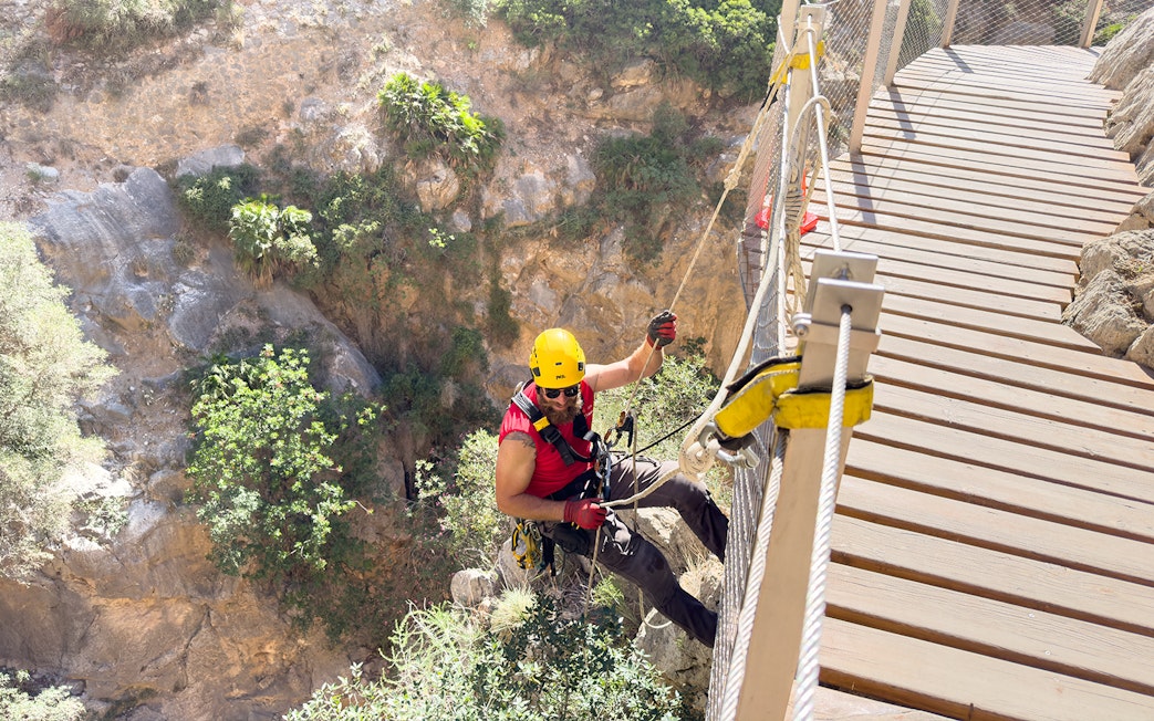 Person rappelling beside a wooden walkway on Caminito del Rey, Spain.