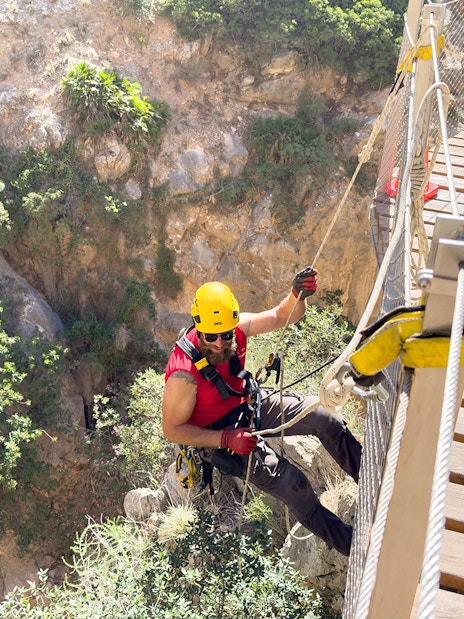 Person rappelling beside a wooden walkway on Caminito del Rey, Spain.