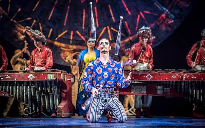 Performer juggling clubs on stage during Luzia show.