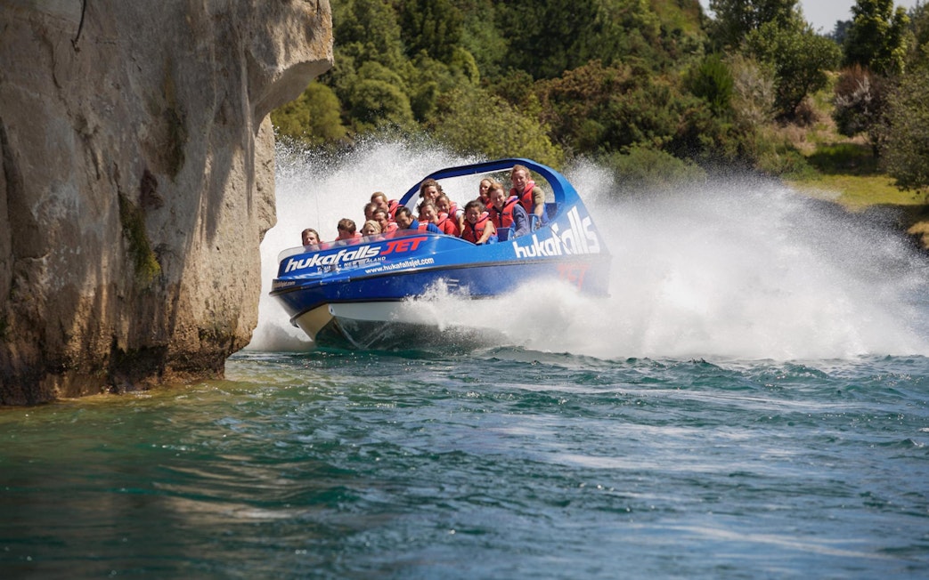 Tourists on a jet boat navigating near rocky cliffs at Huka Falls, New Zealand.
