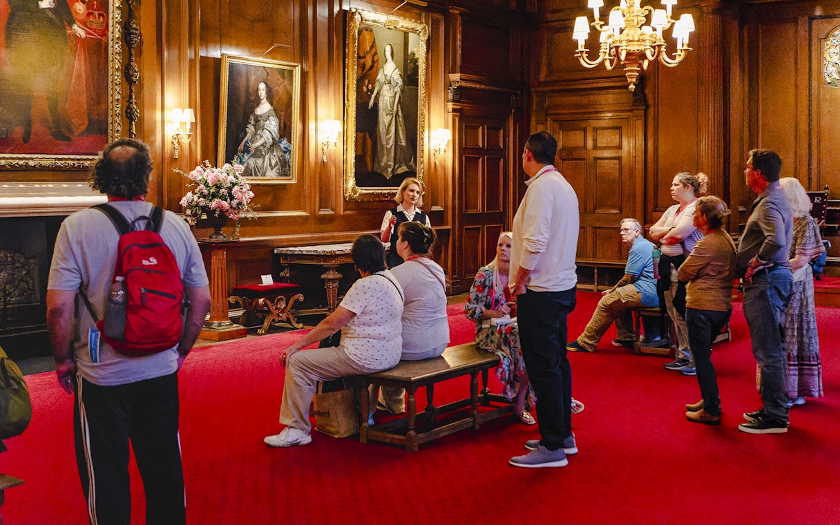 Tour group listening to a guide in the ornate interior of the Palace of Holyroodhouse.