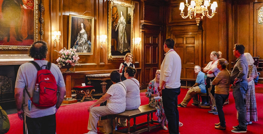 Tour group listening to a guide in the ornate interior of the Palace of Holyroodhouse.