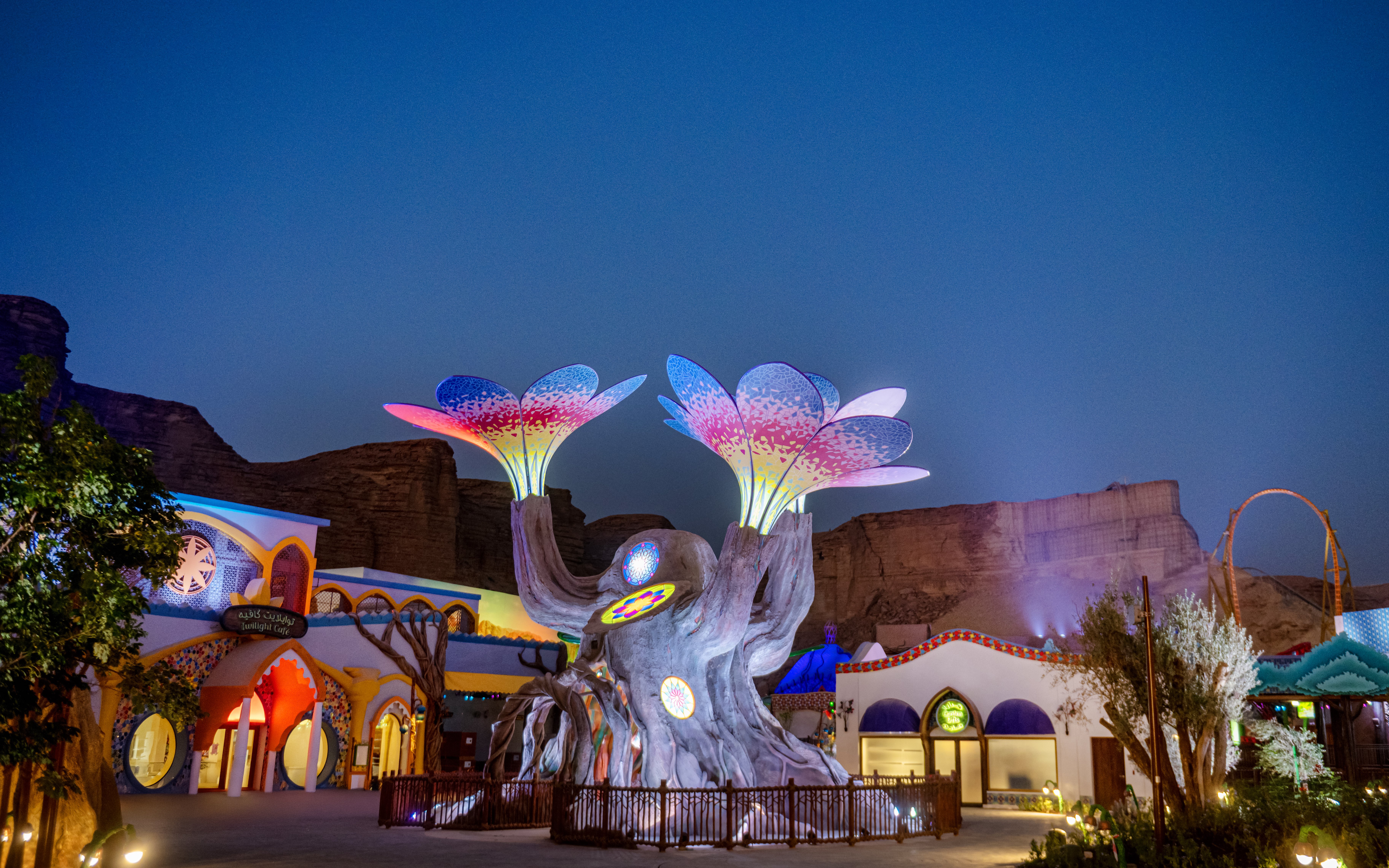 Colorful illuminated tree sculpture at Six Flags Qiddiya City against a twilight sky.
