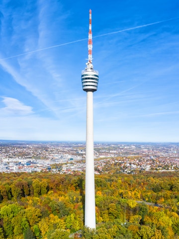 Stuttgart TV Tower rising above autumn trees with cityscape in the background.