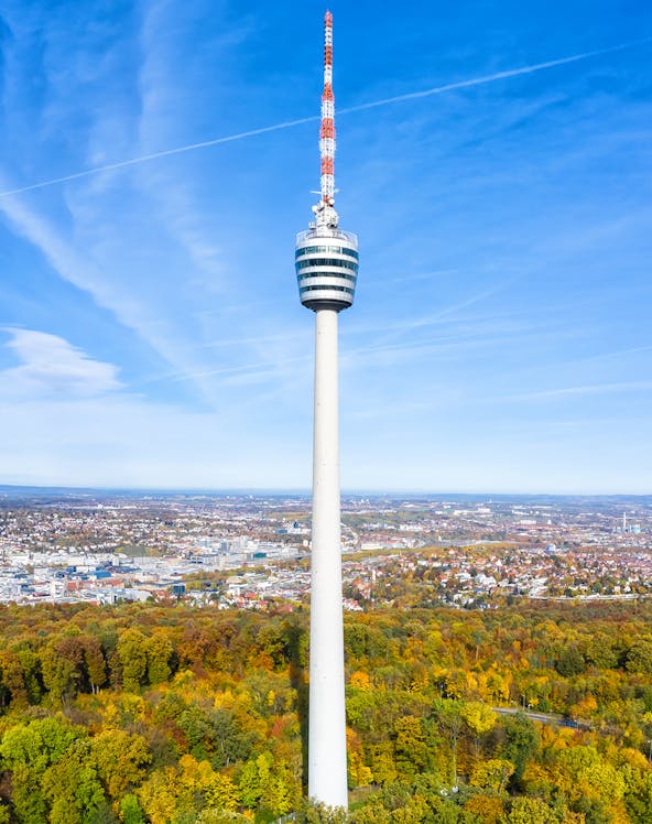 Stuttgart TV Tower rising above autumn trees with cityscape in the background.