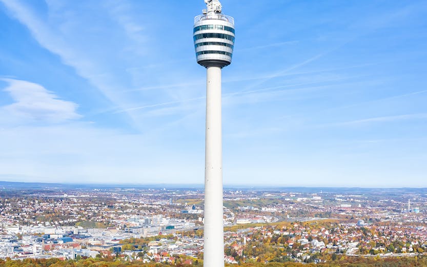 Stuttgart TV Tower rising above autumn trees with cityscape in the background.