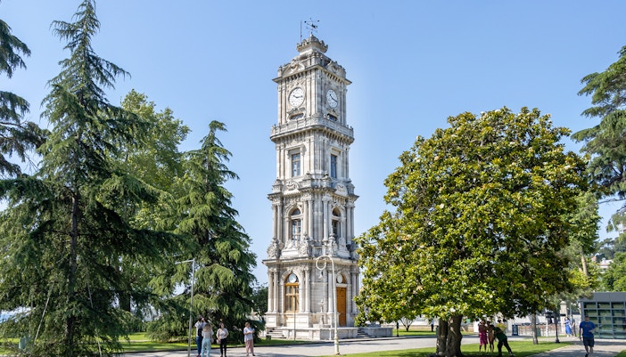 Harem clock tower at Dolmabahce Palace surrounded by trees in Istanbul.