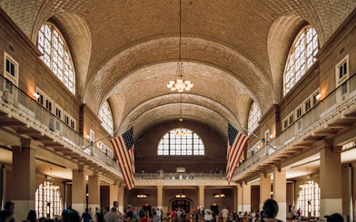 Ellis Island Immigration Hall with American flags and visitors.