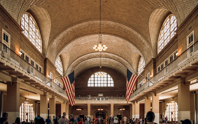Ellis Island Immigration Hall with American flags and visitors.