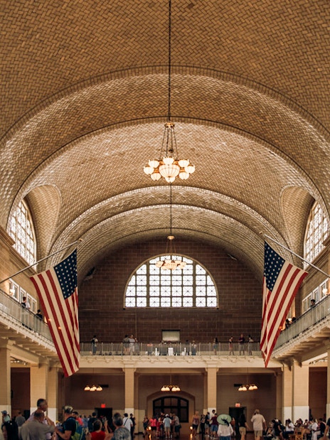 Ellis Island Immigration Hall with American flags and visitors.